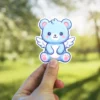 This adorable blue bear with fluffy wings is a waterproof vinyl sticker, perfect as a UV resistant decal for your water bottle or laptop.