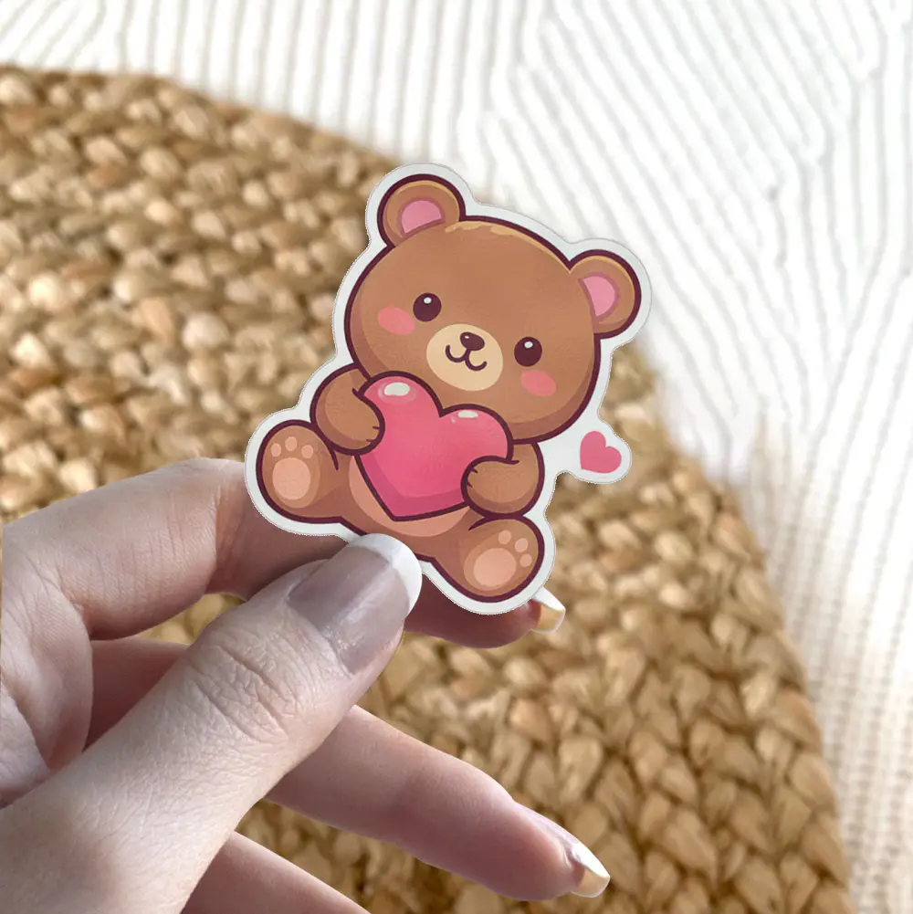 This adorable waterproof vinyl sticker features a kawaii bear hugging a pink heart, perfect as a UV resistant decal for your water bottle or laptop.