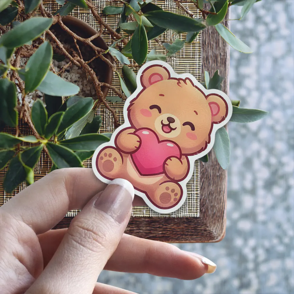This adorable, blushing bear clutching a pink heart is a waterproof vinyl sticker, perfect as a UV resistant decal for your water bottle or laptop.