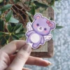 This adorable purple bear with wings and a pink bow is a waterproof vinyl sticker, perfect as a UV resistant decal for your water bottle or laptop.