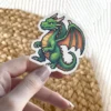 Pixel art dragon sticker, a waterproof vinyl sticker, features vibrant green and orange tones.