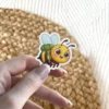 A cute cartoon bumble bee wearing a green backpack and smiling, with light blue wings, captured in a vinyl sticker.