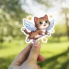 A cartoon tabby cat with blue eyes and white wings is flying joyfully amidst yellow stars.