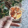 A cute cartoon squirrel with a bushy tail holds an acorn and says 