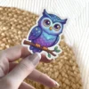A cute owl with a starry night sky design sits on a branch with small green leaves.