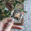 A cute chibi anime character dressed in a dark hooded robe with gold trim is crying profusely, holding their face, with a broken heart and 'H-huh?' text beside them.