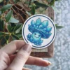 A circular sticker features a cartoon mushroom character with a face, adorned with blue crystals instead of a cap.