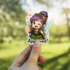 A cute chibi fairy sticker with purple hair, green leaf dress, light blue wings, winking, giving a thumbs up, and saying 'Approved!'