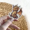 An adorable cartoon fantasy dragon sticker with warm orange and brown scales, small horns, and large leathery wings, perfect for fantasy lovers.