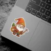 A cheerful cartoon Christmas gnome character with a long white beard, wearing an orange hat and outfit, carrying a small pine tree in a sack on his back and holding a hand axe.
