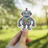 A cute, smiling gray robot sticker with colorful exposed gears on its chest.