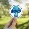 A cute, round, blue glowing mushroom with a smiling face and mystical runes covering its cap, presented as a vinyl sticker.