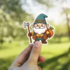 A charming cartoon illustration of a friendly gnome character with a white beard, wearing a green hat, holding an axe, and carrying a sack of carrots.