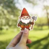A cute cartoon gnome with a red hat, holding an axe and wearing a tool belt, vinyl sticker.
