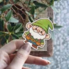 A cute cartoon gnome with a fluffy white beard, green hat, and a tool belt is smiling cheerfully.