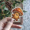 A cute, smiling mushroom character sticker with a knitted texture and white polka dots on its cap.