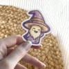 A charming cartoon mushroom wizard sticker with a purple star-spangled hat and robe, a long beard, and a happy waving expression.
