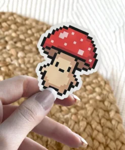 A charming pixel art style mushroom sticker with a red cap and a light brown stem, featuring a simple, friendly face.