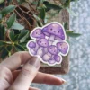 A cluster of adorable purple mushrooms with smiling faces arranged together in a sweet and whimsical design.