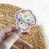 A kawaii mushroom character with a rainbow-spotted cap winks and smiles.