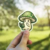 A charming vinyl sticker depicts a cheerful mushroom character engrossed in reading a small book.