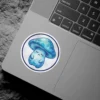 A watercolor-style illustration of a cute, sad blue mushroom with closed eyes and a small body, outlined in dark blue and set against a textured white background, all within a circular border.