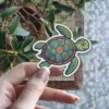 A cute, smiling sea turtle sticker with a detailed mosaic shell featuring colorful floral and nature patterns.