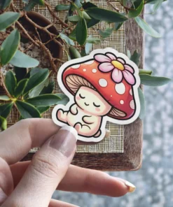 A cute, stylized mushroom character with a red spotted cap and a pink flower, sleeping peacefully with closed eyes.