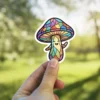 A cute mushroom character with a happy face and rainbow stained glass pattern is held up by a finger.