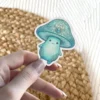 A kawaii teal mushroom character with a gemstone on its cap and ornate swirls on its cap and stem.