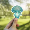 A cute, anthropomorphic mushroom character with a swirling pattern on its cap holds a small lantern in its hand.