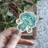 A whimsical sticker depicting a glowing blue and green mushroom adorned with hanging lanterns.