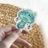 A whimsical sticker depicting a glowing blue and green mushroom adorned with miniature lanterns hanging from its cap.