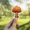 A vinyl sticker depicts a mushroom with a cap shaped like flames and a stem adorned with tribal patterns.