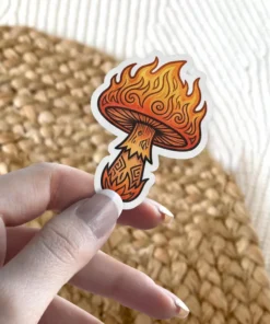 A sticker featuring a mushroom with a cap engulfed in flames and a stem decorated with intricate patterns, all rendered in vibrant orange and yellow hues.