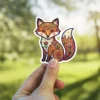 A cute sitting fox is decorated with intricate red, green, and orange folk art floral patterns.