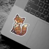 A colorful folk art illustration of a sitting fox, adorned with intricate floral and scroll patterns in warm autumn hues.
