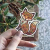 A cute orange fox sticker decorated with colorful folk art style flowers and patterns on its body, head, and tail.