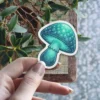 A teal mushroom sticker with a glowing cap and stem, featuring intricate scale-like patterns and delicate gills.