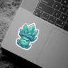 A cartoon sticker of a teal and green crystal mushroom creature with a grumpy expression and pointed facets, outlined in white.