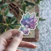 A cute, smiling mushroom sticker adorned with an iridescent cap of purple, pink, and teal colored crystals.