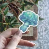 A vibrant blue-green mushroom sticker features a cap with glowing dots, a detailed underside, and a whimsical stem.