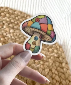 A whimsical sticker depicts a mushroom with a cap and stem made of colorful patchwork fabric squares, accented with three buttons.
