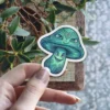 A vibrant blue and green psychedelic mushroom sticker featuring multiple eyes and smiling faces on both the cap and stem.