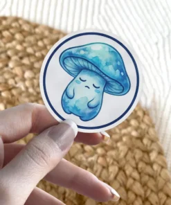 A round sticker features a watercolor-style illustration of a sad, blue mushroom with its eyes closed, set against a white background.