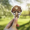 A whimsical steampunk mushroom character with a clock on its cap and gears for its body and arms.