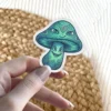 A vibrant vinyl sticker of a trippy mushroom with two sets of eyes and intricate teal and green patterns.