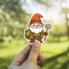 A delightful cartoon sticker featuring a friendly gnome dressed in green, wearing an orange hat, holding an axe.