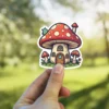 A cartoon sticker of a red and white spotted mushroom house with a cute green caterpillar on the roof.