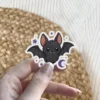 Cute cartoon black bat, large pink ears, tiny white fangs, purple stars, crescent moon, vinyl sticker.